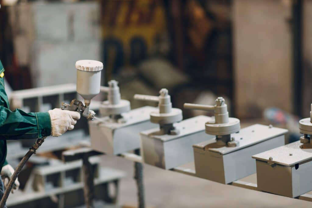 Powder primer coating of metal parts. Worker man in a protective suit sprays powder paint