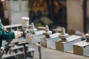 Powder primer coating of metal parts. Worker man in a protective suit sprays powder paint
