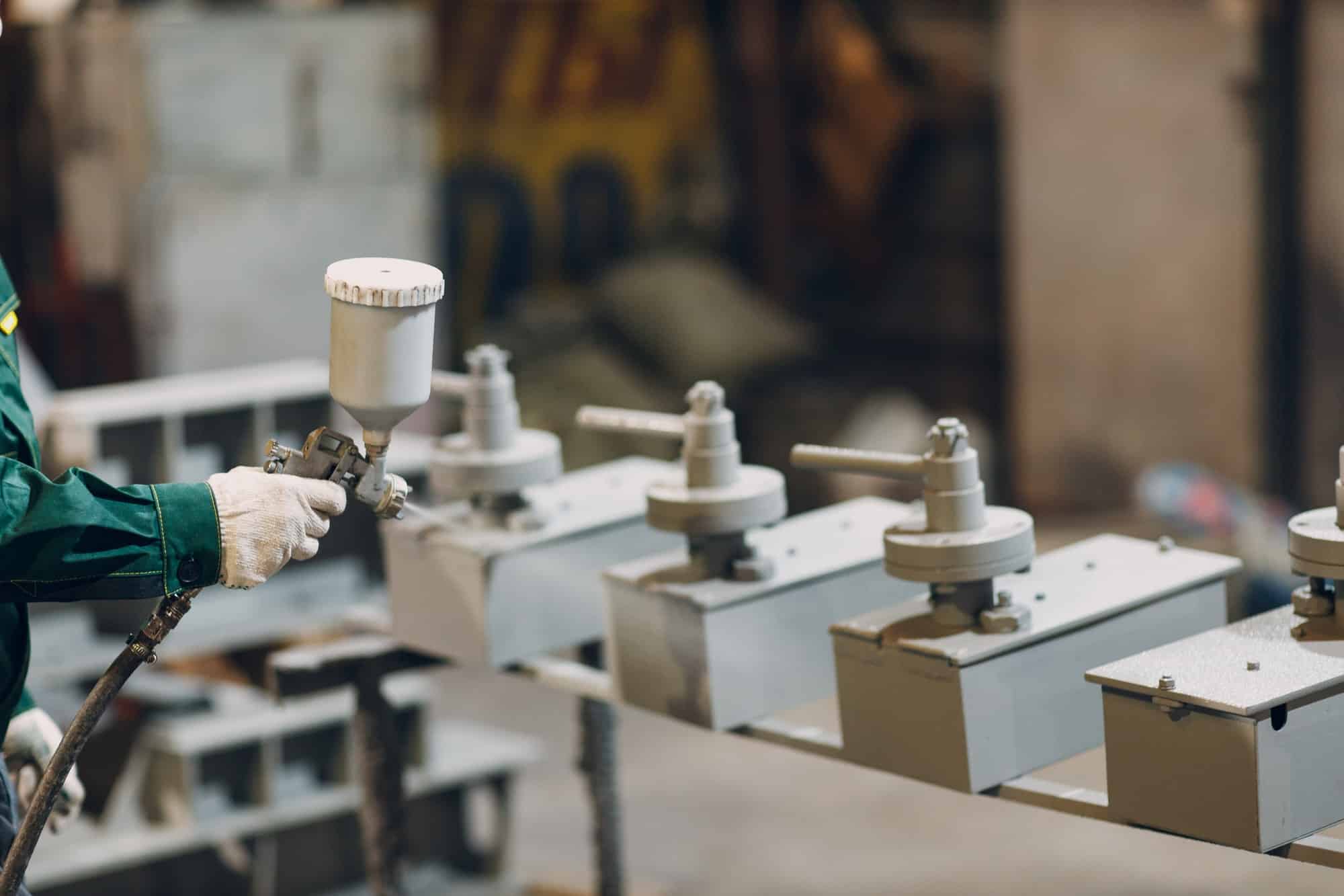 Powder primer coating of metal parts. Worker man in a protective suit sprays powder paint