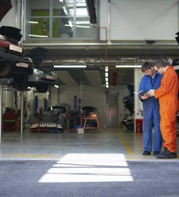 College mechanic students reading manual in repair garage